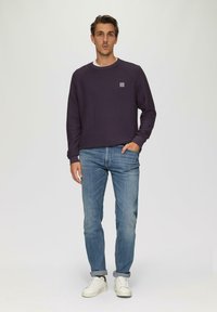 Lila Crewneck-Pullover mit einem strukturierten Muster, getragen über einem weißen Hemd. Kombiniert mit hellblauen Jeans und weißen Sneakers.