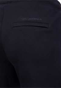Schwarze Jogginghosen aus strukturiertem Material, mit einer Gesäßtasche und dem geprägten Logo "KARL LAGERFELD" über der Tasche.