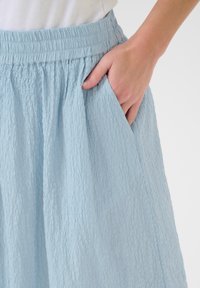 Lyseblå, tekstureret nederdel med elastisk talje og sidelommer, der viser en afslappet, flydende silhuet.