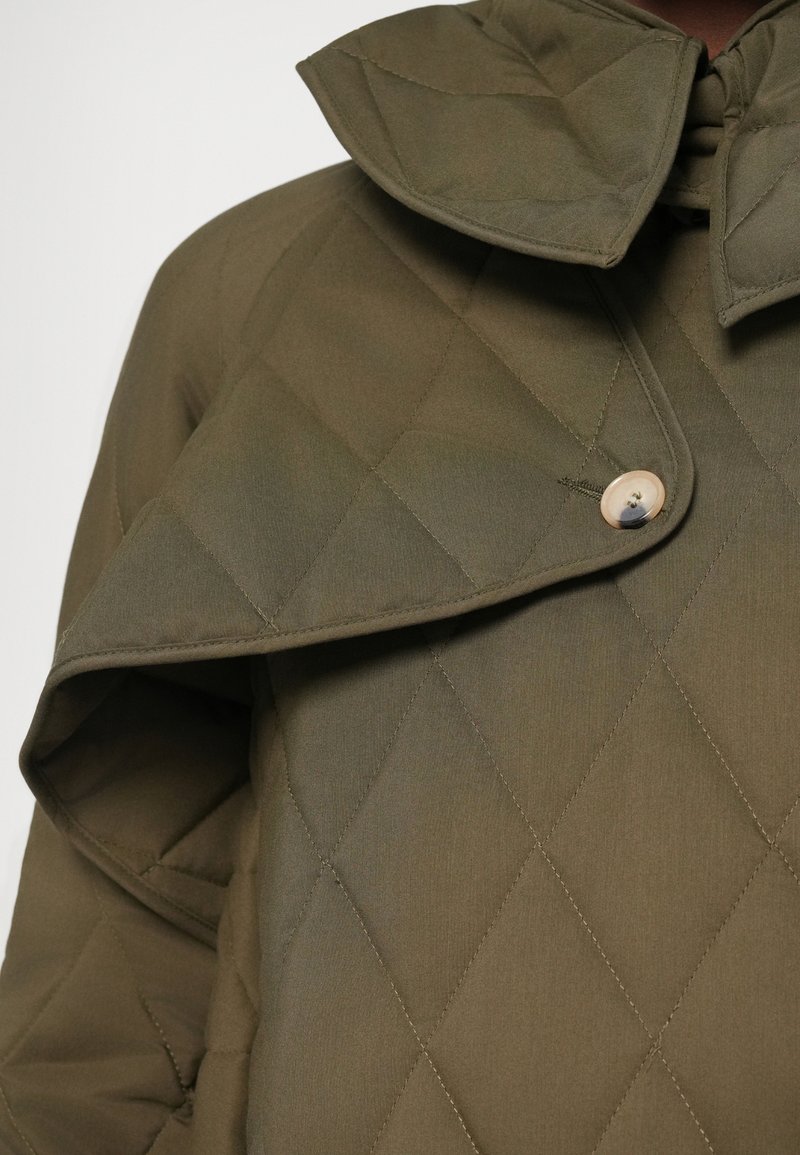 Veste matelassée vert olive avec un matelassage en losanges, un grand rabat de col et un bouton visible près de l'encolure.
