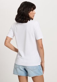 Biała bawełniana koszulka z krótkim rękawem i okrągłym dekoltem, zestawiona z jasnoniebieskimi szortami dżinsowymi z postrzępionym dołem.