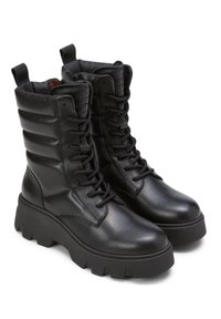 Schwarze Lederkampfstiefel zeichnen sich durch eine Höhe bis zur Mitte der Wade, eine wuchtige Plateausohle, eine Schnürung an der Vorderseite und eine gesteppten Detailgestaltung am Schaft aus.