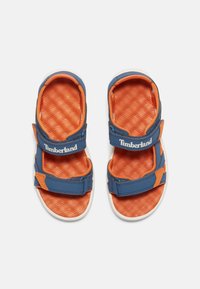 Sinine ja oranž sandaalid tekstureeritud oranži tallaga, siniste rihmade ja valgete talladega. Omavad reguleeritavaid rihmasid ja Timberlandi logo.