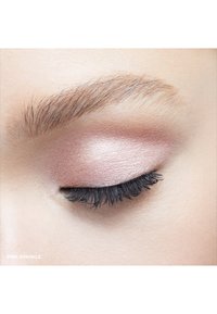 Nahaufnahme eines Auges mit beigem Lidschatten und dicken schwarzen Wimpern. Subtiler Schimmer im Lidschatten. Die Haare sind hellbraun mit feiner Textur.