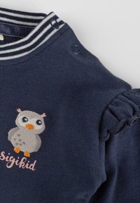 Navy blue cotton shirt with striped collar, featuring a gray owl embroidery and pink text reading "Sigikid." Ruffled sleeve details.