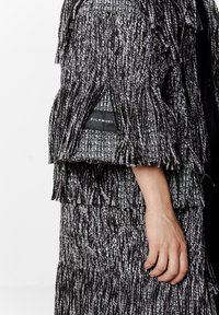 Kurtka czarno-biała o fakturze frędzli z tkanym wzorem, z widoczną metką marki i luźnym, warstwowym krojem.