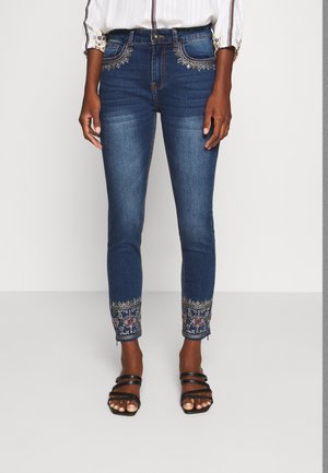 Jeans de mezclilla azul oscuro con intrincados bordados florales en el dobladillo. Diseño slim fit, que presenta un cierre de botón y un desgaste mínimo.