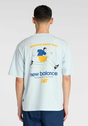 Camiseta de algodón color azul claro con un gráfico de carrera y el logo de "New Balance" en la parte trasera. Manga corta y corte relajado.