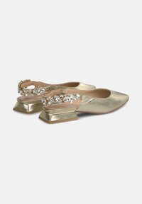Scarpe slingback metalliche dorate con punta a punta e tacco largo. Caratterizzate da una cintura decorativa adornata con gemme trasparenti e accenti dorati.