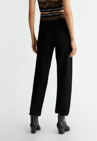 Czarne dzianinowe spodnie o zwężanym kroju, z elastycznym paskiem w talii, w połączeniu z czarnymi botkami za kostkę, prezentującymi teksturowane wykończenie.