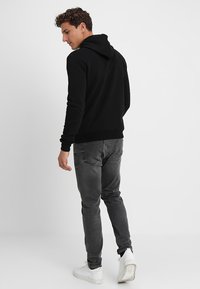 Zwarte hoodie met een ontspannen pasvorm, voorzien van een kangoeroezak en ribgebreide zoom. Gecombineerd met grijze slim-fit jeans en witte sneakers.