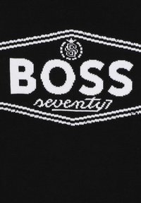 Maglione nero lavorato a maglia con un logo bianco "BOSS" in evidenza e il testo "seventy7", con linee decorative bianche sopra e sotto.