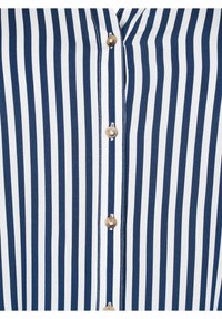 Chemise rayée bleu marine et blanche avec un col boutonné, des boutons dorés et une texture de tissu lisse avec des coutures contrastées.