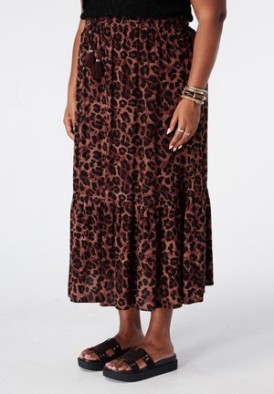 Femme portant une jupe midi marron et noire à imprimé léopard, des sandales noires sans bride et des bracelets au poignet gauche.
