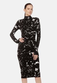 Czarna sukienka z długim rękawem, z białym wzorem rozpryskującej się farby w stylu abstrakcyjnym, dopasowana, z wysoką szyją i otworami na kciuki w rękawach.