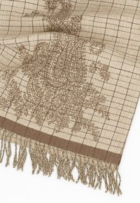 Tessuto beige con un intricato design paisley marrone e motivo a griglia, caratterizzato da frange decorative ai bordi. Texture morbida e materiale tessuto.