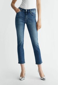 Temno modri jeans z visokim pasom, ožji kroj, pet žepov in skrajšanimi hlačnicami, v kombinaciji s srebrnimi visokimi petami.