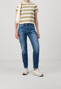 Avskuren randig t-shirt i krämfärg och olivgrön, ihopparad med åtsittande blåjeans och beige sneakers. En enkel, avslappnad outfit.