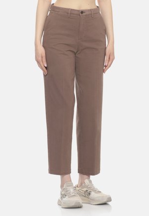 Pantaloni marroni a gamba dritta indossati da una persona in piedi con sneakers beige su sfondo bianco.