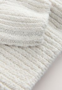 Gros plan d'un tissu tricoté blanc et doux montrant un motif côtelé texturé et des fibres de fil épaisses créant une surface textile confortable.