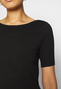Černý krátký rukáv top s širokým, zaobleným výstřihem. Vyrobeno z lehkého, texturovaného materiálu. Švy na ramenech.
