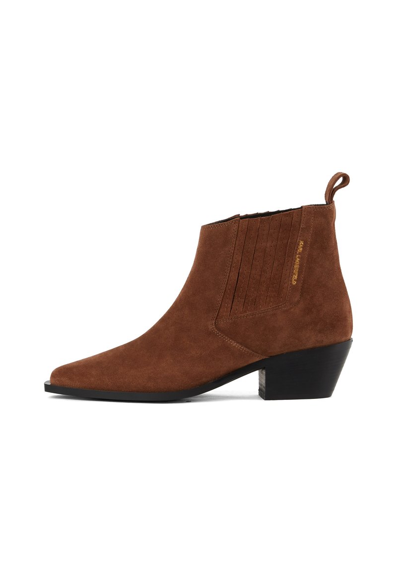 Botine din suede maro, cu vârf ascuțit, panouri laterale texturate și un toc bloc mic. Prezintă o mici buclă de prindere în spate.