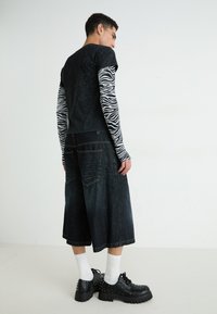 Camiseta negra de manga corta sobre una camisa larga de estampado de cebra, combinada con shorts de denim oscuro y zapatos negros con tachuelas. Calcetines blancos visibles.