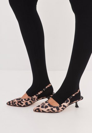 Leopardikuosi slingback-korkokengät, joissa on terävä kärki, mustat yksityiskohdat ja kapea korko, yhdistettynä ribattuihin mustiin sukkahousuihin.