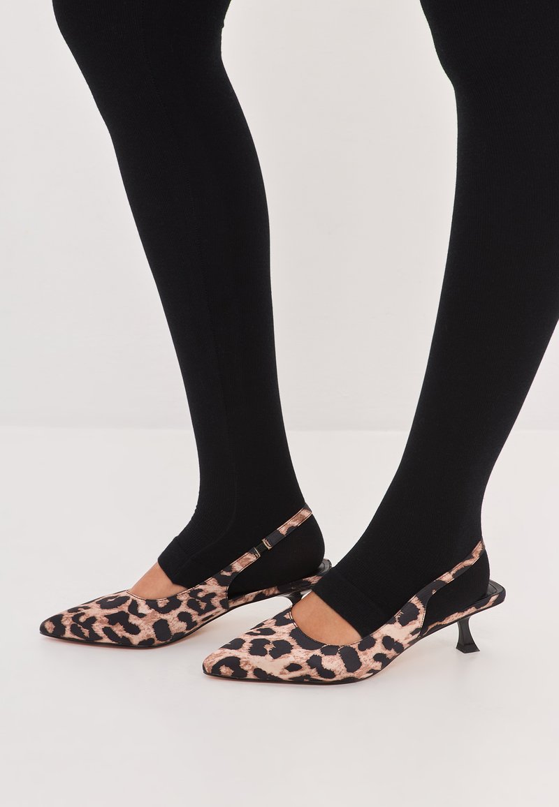 Leopard print slingback heels with a pointed toe, black accents, and a slim heel, paired with ribbed black tights.