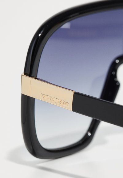 Black oversized sunglasses with gradient lenses, featuring a gold accent on the temple with engraved brand name, smooth plastic texture.