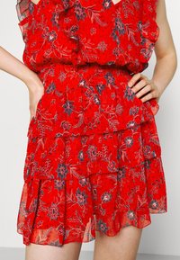 Rotes Blumenkleid mit gestuften Rüschen, leichtem Stoff, marineblauen Blumenmustern und tailliertem Schnitt. Weiche, semi-transparente Textur.
