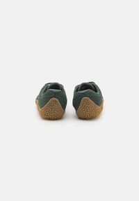Scarpe Merrell verdi con suola in gomma ruvida e tomaia in mesh. Presentano un design a profilo basso e un'area del tallone rinforzata per supporto.