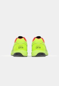 Zelene tenisice za trčanje sa glatkom teksturom, s crnim potplatom, sivoj naglascima i crvenim jastučićem za petu. Logo "adizero" nalazi se na stražnjem dijelu.