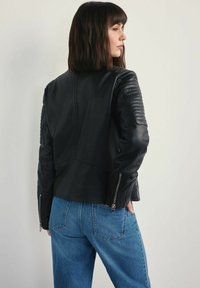 Czarna skórzana kurtka motocyklowa z pikowanymi akcentami na ramionach i mankietami na zamek, w połączeniu z niebieskimi jeansami w wysokim stanie. Gładka tekstura i dopasowany krój.