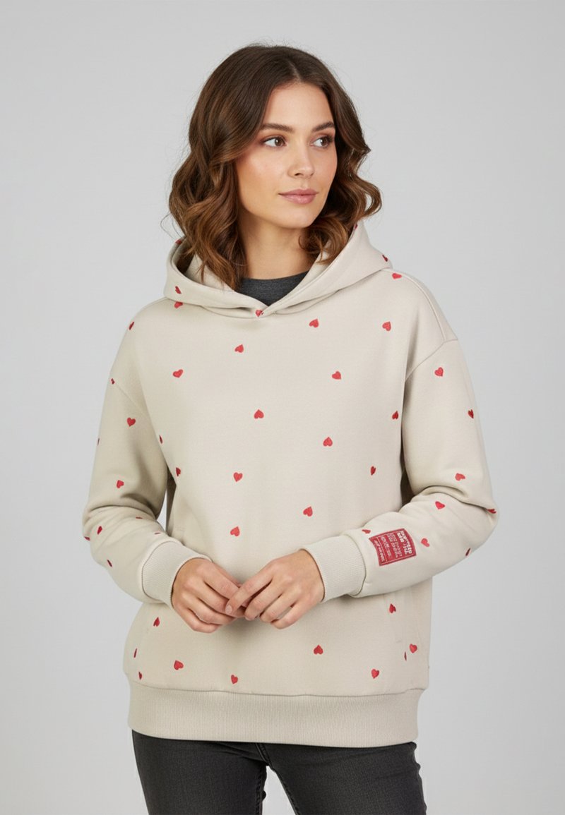 Beige Kapuzenpullover mit roten Herzmustern, gerippten Bündchen und einem Label-Akzent am Ärmel. Weicher Stoff mit entspanntem Schnitt.