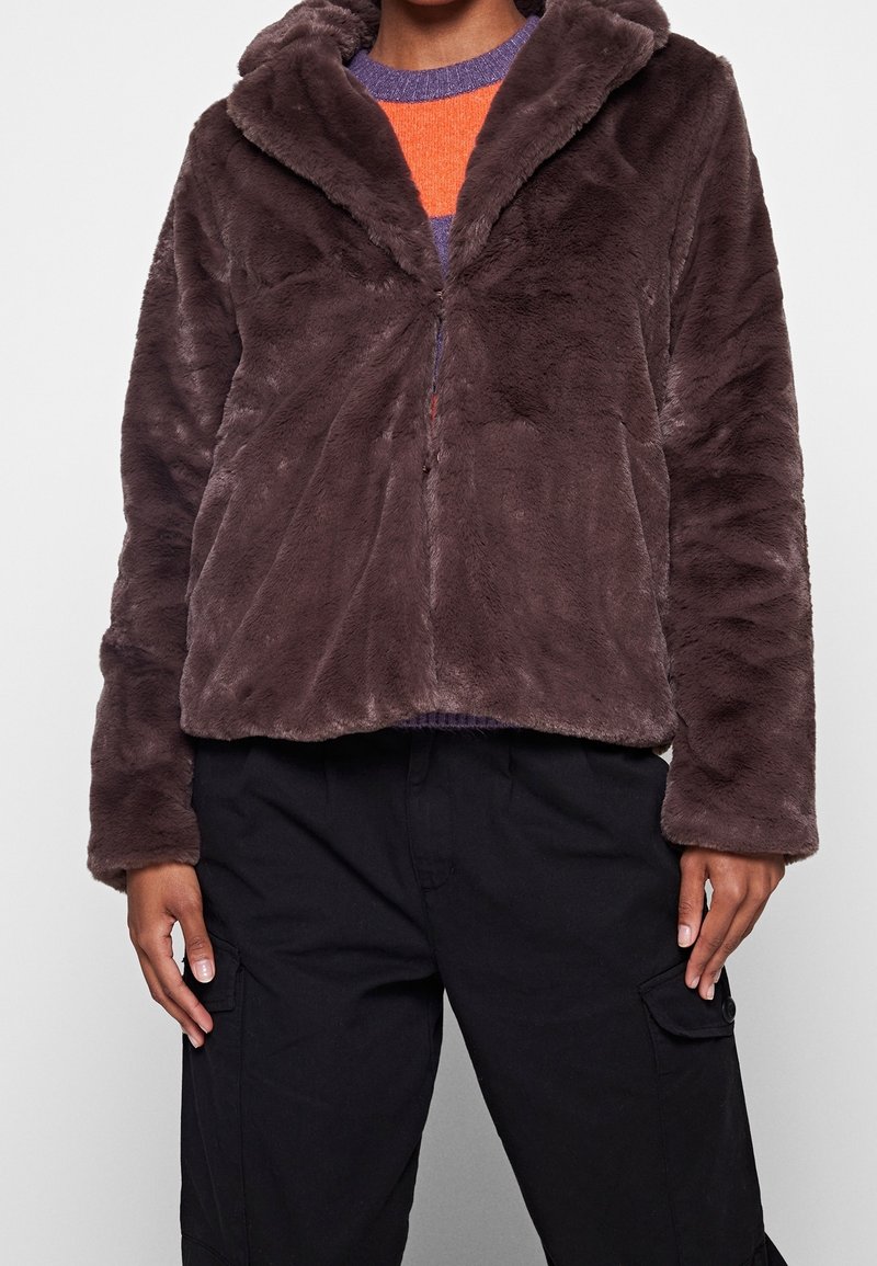 Brown faux fur jacket with a hood, zip closure, and long sleeves. Soft texture, slightly cropped design, paired with black cargo pants.