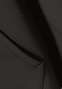 Tessuto nero con una texture liscia, caratterizzato da una cucitura visibile e una piccola tasca. Il materiale appare flessibile e fitto.