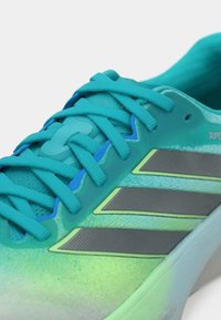 Chaussure de sport turquoise avec tige en mesh, lacets texturés et trois bandes argentées. Dégradé de couleurs avec des accents verts.