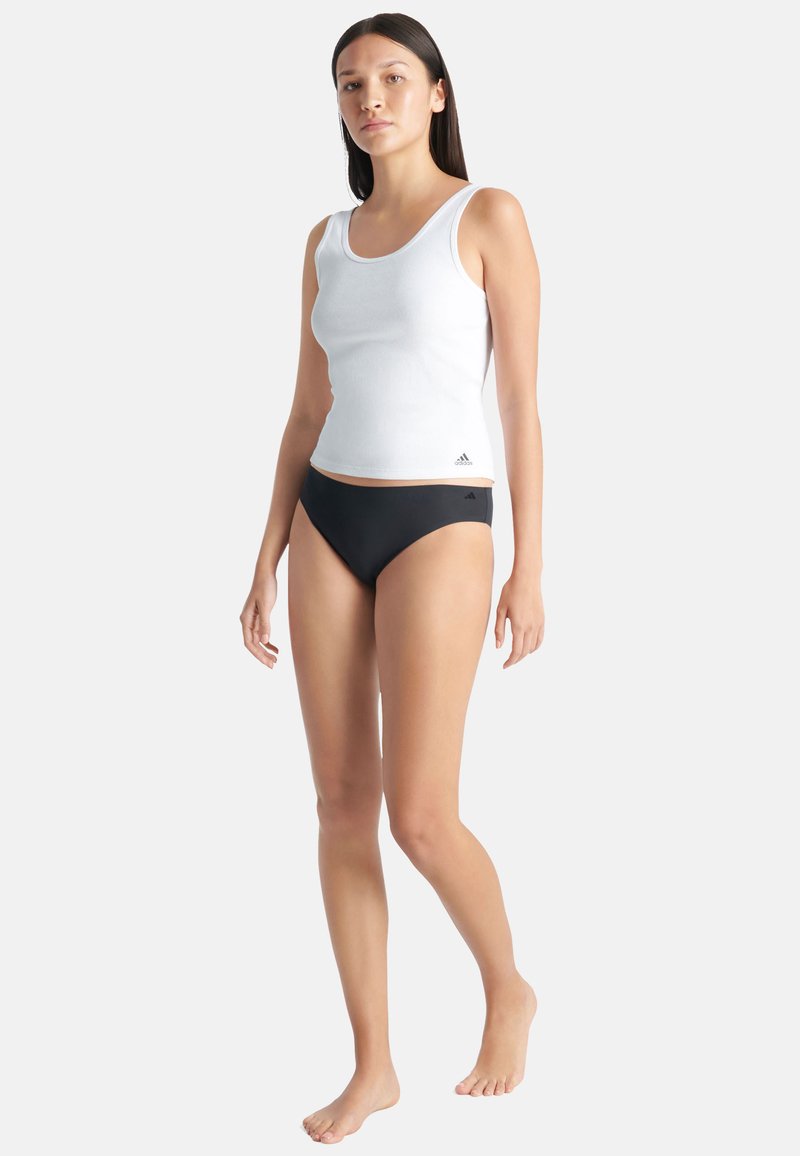 Wit geribbelde tanktop en zwarte bikini-broekjes. De tanktop heeft een ronde hals en is gemaakt van rekbare stof. De bikini heeft een gladde textuur.