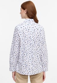 Camicia bianca con un motivo di forme astratte blu e blu scuro, maniche lunghe, colletto button-down e una vestibilità leggermente over.