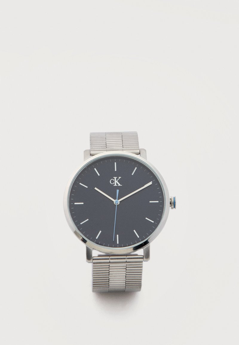 Montre-bracelet Calvin Klein avec cadran noir, index des heures en argent, bracelet en maille argentée, et trois aiguilles indiquant 10:09:29.