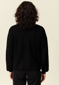 Svart stickad tröja med avslappnad passform, sänkta axlar och långa ärmar. Har en ribbad struktur och rak nederkant, bärs över svarta byxor.