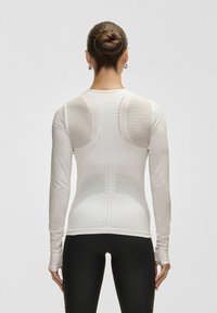 Långärmad, åtsittande topp i ljuskräm med ventilerande mesh-paneler, strukturerad design och en slät finish, i kombination med svarta leggings.