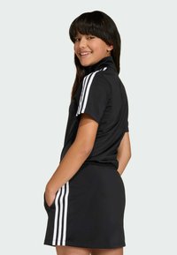 Czarny strój sportowy z wysokim kołnierzem i krótkim rękawem. Posiada białe paski na rękawach i bokach, fakturowany materiał oraz kieszenie.