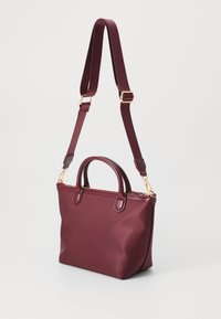Burgundy handbag made of smooth synthetic material, featuring two top handles, an adjustable strap, and gold-tone hardware accents.