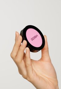 GOSH blush compact featuring a smooth, round, black plastic case with a bright pink powder inside, held in a hand.
