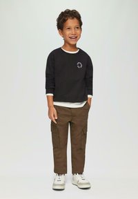 Zwarte sweatshirt met witte kraag, voorzien van een kleine circulaire afbeelding. Bruine cargo broek met zijzakken, grijs en witte sneakers.