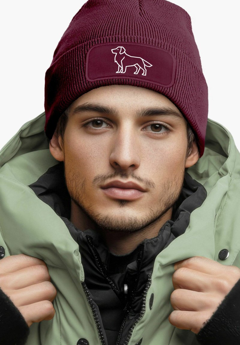 Maroon beanie with textured knit and a patch featuring a white dog silhouette; paired with a mint-green, zippered outer jacket.