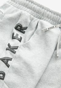 Pantalones de chándal grises con una tela texturizada. Presentan un estampado de logo en negro en el lateral y una cintura elástica con cordón para ajustarse.