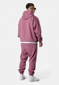 Hooded sweatshirt and joggers in soft pink fabric, relaxed fit, ribbed cuffs, and hem, paired with white sneakers.